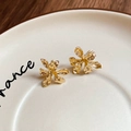 Macro detail of golden 3D flower stud earrings featuring textured metal pleats on a dish - Gold