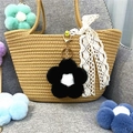 Plush flower bag charm with colorful petals and gold keychain on a straw handbag - Black