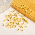 Gefacetteerde 14K goudgevulde kralen verspreid op wit oppervlak met houten dienblad erbij - 2.5mm / 18K Goud
