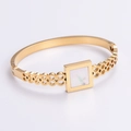 Detalle macro de pulsera rígida geométrica dorada con incrustación de nácar blanco - Dorado