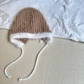 Close-up of brown plush earflap hat with white trim and tassels on a soft knit blanket - 3-6 Years / Khaki