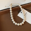Gros plan d'un collier de perles avec fermoir doré dans un écrin en velours marron - 12mm / Blanc