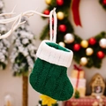 Groene kabelgebreide kerstkous met witte omslag hangend aan een feestelijke tak - Groen