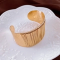 Detail van een brede gouden manchetarmband met gepolijste afwerking en metaaldraadtextuur - Goud