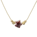 Détail d'un pendentif étoile en céramique avec glaçure rouge et blanche sur chaîne dorée - Cuivre et Étoile Sarcelle Claire