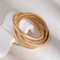 Détail d'un bracelet spirale doré multicouche sur pierre blanche aux ombres douces - Bracelet enveloppé de chaîne de serpent multicouche doré