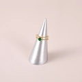 Detalle de anillo dorado con gema verde sobre un soporte de anillo cónico plata - Plateado