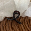 Detailed view of a twisted dark brown hair claw clip on a rustic woven rattan mat - Bright Amber