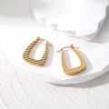 Detailed view of golden geometric earrings with textured diagonal stripes on white stand - Textured Trapezoid