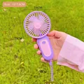 Portable mini USB rechargeable fan in purple and pink, held against a green grass background - Purple