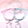 Paar gewebte Armbänder in Pink und Blau mit Sternanhängern auf einem rosa Netzhintergrund - Lutscher Liebe (2er-Set - Buntes Seil)