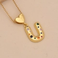 Detailed close-up of golden letter U pendant with colorful zircon stones on a fine chain - Letter U / Gold