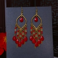 Detail of bohemian gold tassel earrings featuring red waterdrop beads on a dark base - Red Gold
