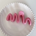Pink wavy hair claw clip made of glossy acrylic on a decorative white ceramic plate - Pink