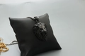Close-up of black lion head pendant with silver chain on a black display cushion - Fashion Black