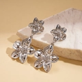 Detail of silver metallic floral earrings with 3D petals on a beige marble surface - Silver