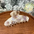Detailed view of beige marble acetate hair claw clip on a wooden tray with festive background - White Starry Purple - Round Top 8-Teeth