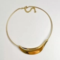 Dettaglio di un ciondolo a mezzaluna dorato lucido su una collana rigida minimalista - Choker Oro