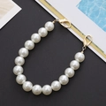 Detail van witte parelketting met gouden karabijnsluitingen op een donkere achtergrond - 14mm Parel Handketting (K143)