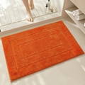 Lebendige orangefarbene saugfähige Badematte mit weicher Plüschtextur auf Fliesenboden - Orange