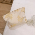 Detail of cream jacquard makeup bag with yellow bow patterns on soft quilted bedding - Wheat
