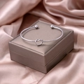 Macro view of a polished silver knot cuff bracelet resting on a silk jewelry box - Silver Knot Style