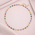 Golden stainless steel evil eye necklace with colorful beads on pink fabric background - Colorful