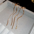 Detailed view of long gold bow earrings with snake chain tassels on grey velvet - Gold Bowknot Snake Chain (HE19718)