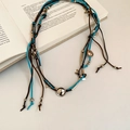 Detail of bohemian suede cord necklace with silver pendants over an open book - Silver-Blue-Coffee