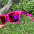 Detail view of pink polarized sports sunglasses with mirrored lenses held outdoors - Matte Pink / Mirrored Red-Purple Lens