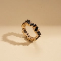 Dettaglio ravvicinato di anello eternity dorato con gemme nere rettangolari e diamanti - Oro