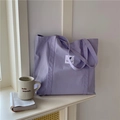 Detail view of purple canvas tote bag featuring a white woven label and durable shoulder straps - Purple