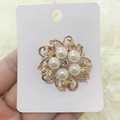 Dettaglio di una spilla a fiore dorata con perle bianche e strass centrale scintillante - Fiore a sei perle