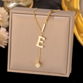 Detail view of gold letter E pendant and small cube on a minimalist steel necklace - Letter E-Gold