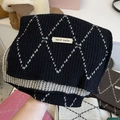 Close-up of a thick knit scarf with black and white diamond patterns and hand made label - Black