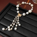 Dettaglio del bracciale di perle con ciondolo a quadrifoglio dorato e nappe eleganti - Oro Bianco