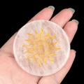 Polished rose quartz energy stone disc with gold sun and eye engraving held in hand - White Crystal Sun