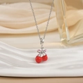 Close-up of a silver necklace with red cherry pendant and a pink bow on fabric - Silver Red Cherry with Pink Bow