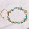 Elegant gold bracelet with square blue zircons displayed on white textured fabric - Sea Blue - Gold