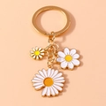 Primer plano de llavero dorado con colgantes de margaritas en esmalte blanco y amarillo - Blanco