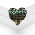 Macro shot of an emerald heart brooch with black crystals on a white pedestal - Green