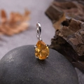 Macro shot of a teardrop-shaped citrine pendant on a silver base over dark stone - Natural Citrine Water Drop Pendant Silver