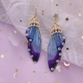 Makroaufnahme von lila Schmetterlingsflügel-Ohrringen mit Strasssteinen und goldenen Haken - Edel Blau Violett Strass-Gold