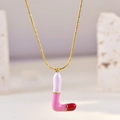 Detail of gold chain necklace featuring an L-shaped lipstick pendant in pink and purple enamel - L
