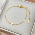 Polished gold stainless steel bracelet with three heart pendants on grey jewelry box - Gold