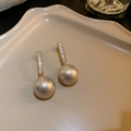 Detailansicht goldener Perlenohrringe mit Zirkoniasteinen auf einer beigen Schale - Champagnerfarbener Langer Zirkonstab Perlenstil