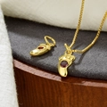 Detailed macro of a gold baby feet pendant with a red zircon on a grey velvet base - Red