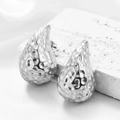 Orecchini a goccia martellati in acciaio inossidabile argento su sfondo di seta - Goccia d'Argento Martellata Densa