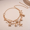 Detail of layered gold starfish and conch body chain with white pearls on beige background - Waist Chain-Gold