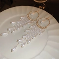 Detalle de pendientes dorados con borlas de perlas y cristales en un plato blanco - Ganchos para la Oreja con Borla de Perlas Doradas
